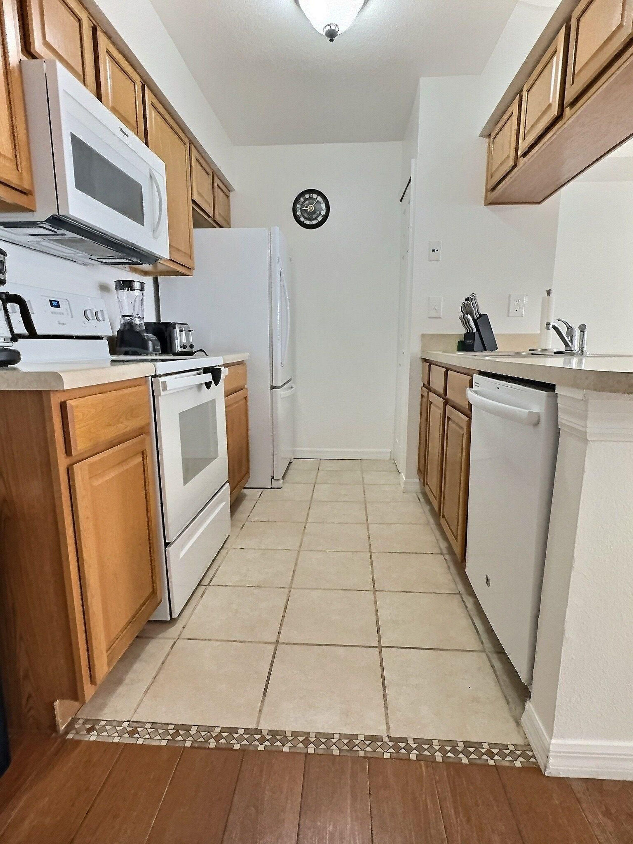 A kitchen with wooden cabinets, a microwave, stove, refrigerator, dishwasher, and a clock on the wall.