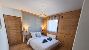Une chambre avec un plancher en bois, un lit avec une literie blanche, deux tables de chevet avec des lampes et une fenêtre avec des rideaux.