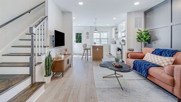 A modern living room with a staircase, a kitchen, and a dining area.