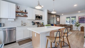 A modern kitchen with white cabinetry, a central island, bar stools, and pendant lighting.