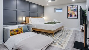 A modern bedroom with a bed, a sofa, a TV, and a ceiling fan.