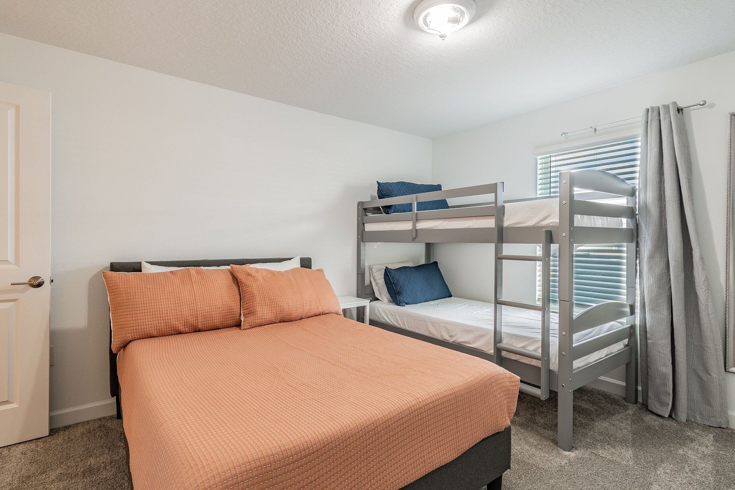 A bedroom with a bunk bed, a single bed, and a window with blinds.