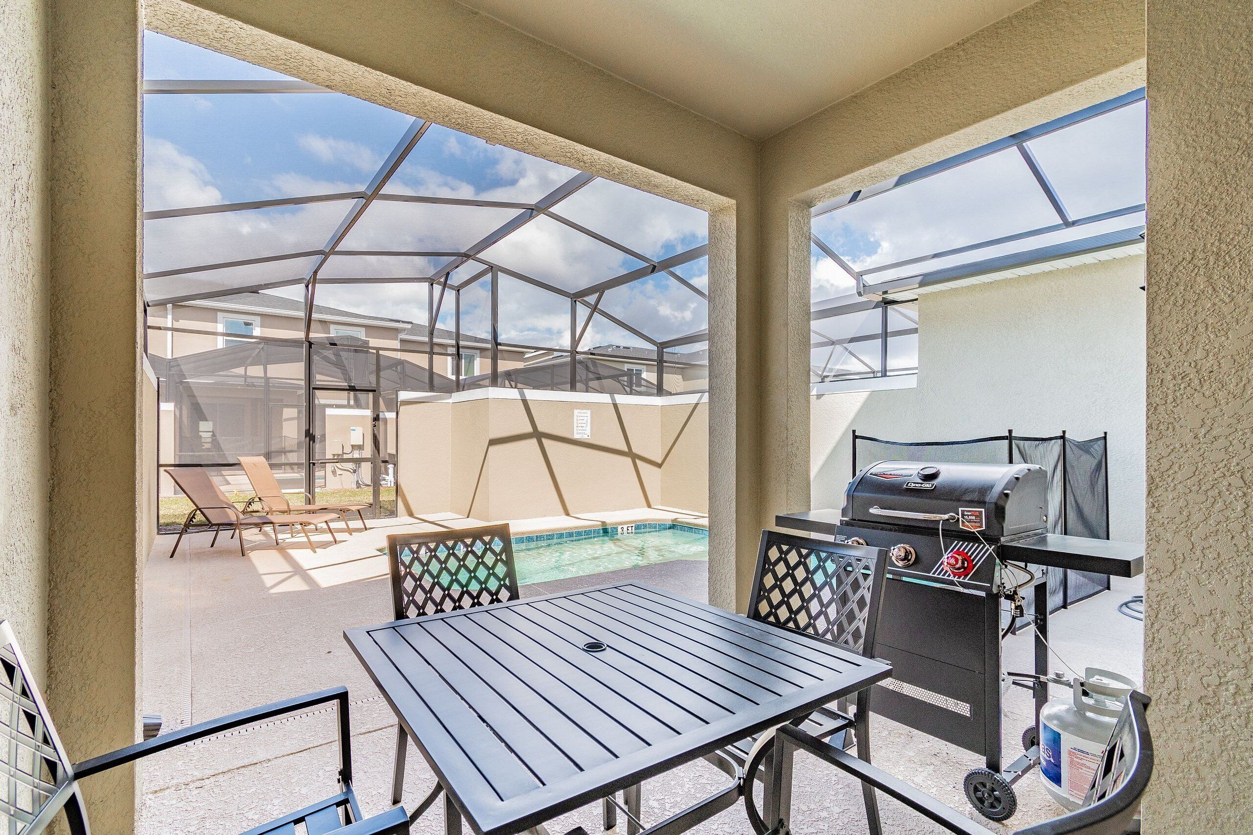 Un patio abrité avec un barbecue, une piscine et des chaises longues.