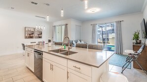 A modern kitchen with a central island, built-in appliances, pendant lighting, and a view to a balcony. - Luxury 4bd/3ba Home Storey Lake (Kissimmee)