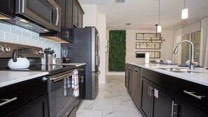 Una cocina moderna con armarios oscuros, electrodomésticos de acero inoxidable, salpicadero de mármol y un jardín vertical verde.