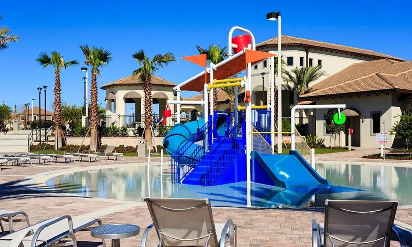 A pool area with a water slide, lounge chairs, and a building with a tiled roof in the background.