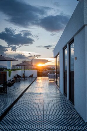 A rooftop terrace with a patterned floor, outdoor seating, and a view of the sunset. - Depa en Colonia Americana | Lapso at Alarcón (Guadalajara)