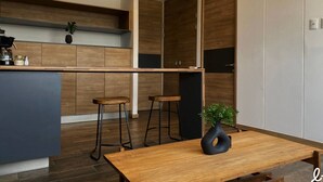 Une cuisine moderne avec des meubles en bois, un îlot central, deux tabourets de bar et une plante en pot posée sur la table.