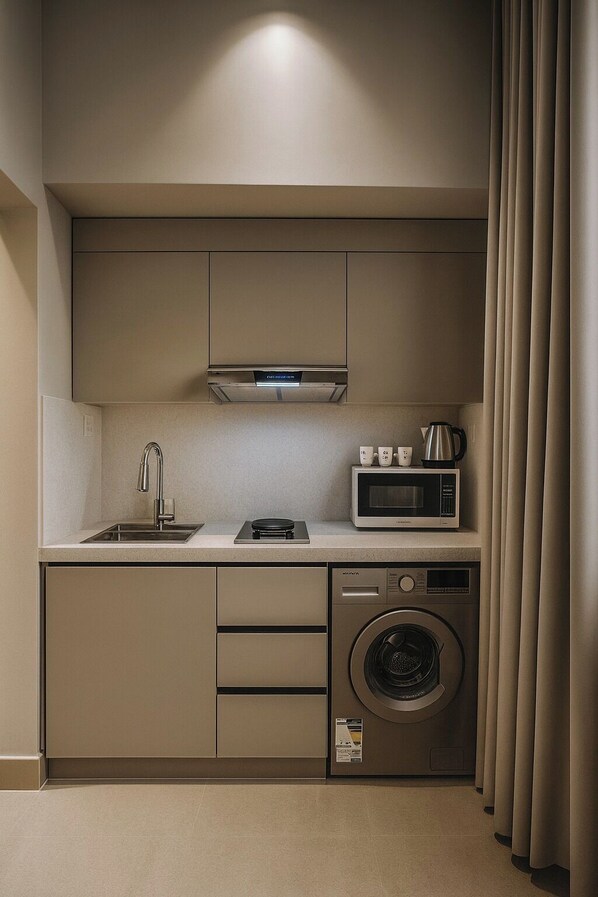Une cuisine compacte équipée d’un four à micro-ondes encastré, d’une plaque de cuisson, d’un évier et d’un lave-linge.