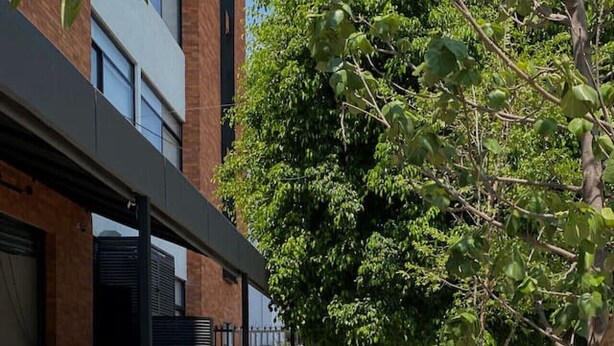 A narrow sidewalk flanked by buildings with a metal fence on one side and a tree-lined path on the other. - Depa con Jardín en la Americana | Lapso at Alarcón (Guadalajara)