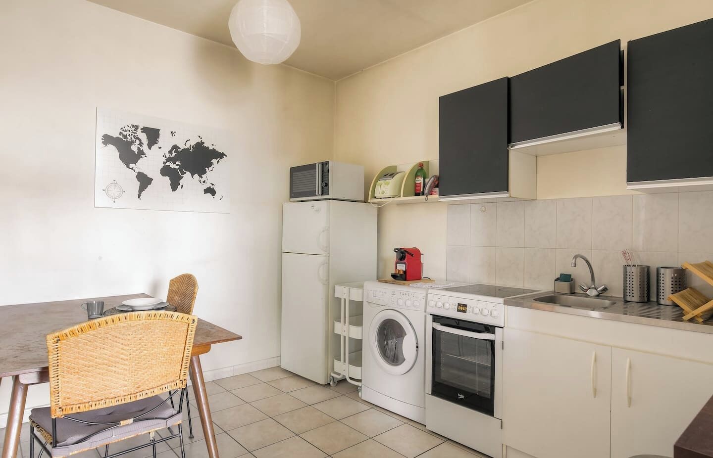 Une cuisine compacte équipée d’un lave-linge, d’un four à micro-ondes et d’un petit coin repas avec une chaise.