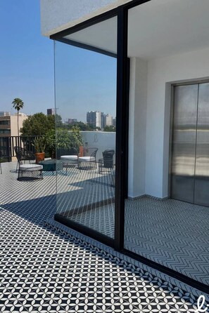 A modern apartment with a large sliding glass door leading to a rooftop terrace with a patterned floor and outdoor furniture. - Loft con balcón en la Americana | Lapso at Alarcón (Guadalajara)