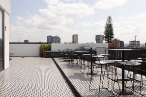 A rooftop terrace with a patterned floor, outdoor seating, and a view of the city skyline. - Loft con balcón en la Americana | Lapso at Alarcón (Guadalajara)