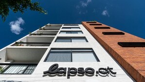 A modern building with a white facade and a wooden accent wall. The name "lapse.at" is visible on the facade. - Loft con balcón en la Americana | Lapso at Alarcón (Guadalajara)