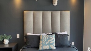 A modern bedroom with a tufted headboard, a bedside plant, and a decorative wall-mounted headpiece. - Loft con balcón en la Americana | Lapso at Alarcón (Guadalajara)