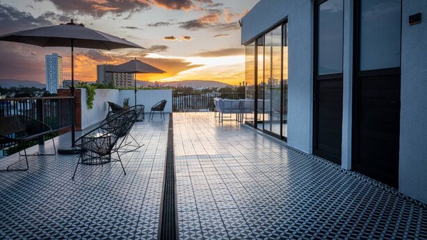 A rooftop terrace with a patterned floor, outdoor furniture, and a sunset view. - Loft con balcón en la Americana | Lapso at Alarcón (Guadalajara)