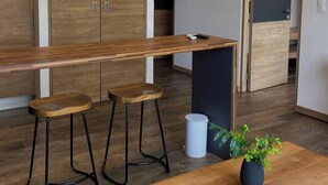 A modern kitchen with wooden cabinets, a long countertop, and two stools. - Loft con balcón en la Americana | Lapso at Alarcón (Guadalajara)