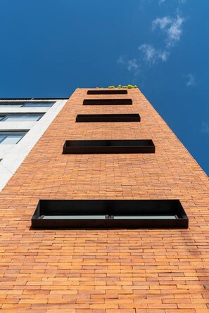 A tall brick building with multiple rectangular windows. - Loft con balcón en la Americana | Lapso at Alarcón (Guadalajara)