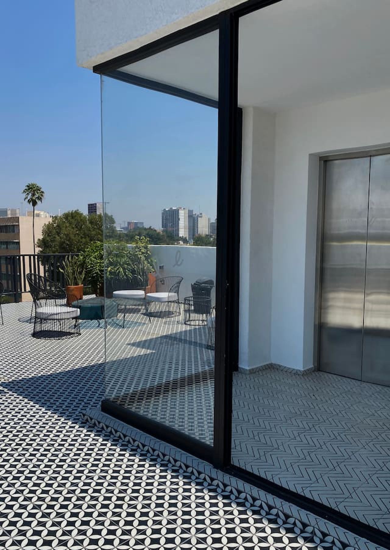 A modern balcony with a patterned floor, a glass door, and outdoor furniture.
