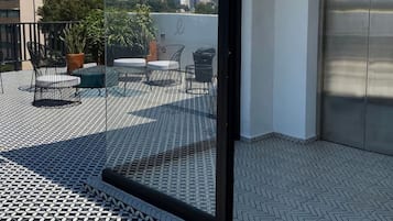 A modern balcony with a patterned floor, a glass door, and outdoor furniture.