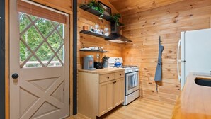 A compact kitchen with wooden walls, a stove, a coffee maker, and a refrigerator. - Story Land- Fall Foliage - Attitash - Fire Pit (Bartlett)
