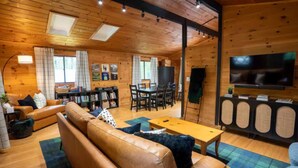 A cozy cabin interior with a leather sofa, a dining table, and a TV. - Story Land- Fall Foliage - Attitash - Fire Pit (Bartlett)