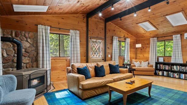 A cozy cabin interior with a stone fireplace, leather sofas, a wooden coffee table, and a bookshelf. - Story Land- Fall Foliage - Attitash - Fire Pit (Bartlett)