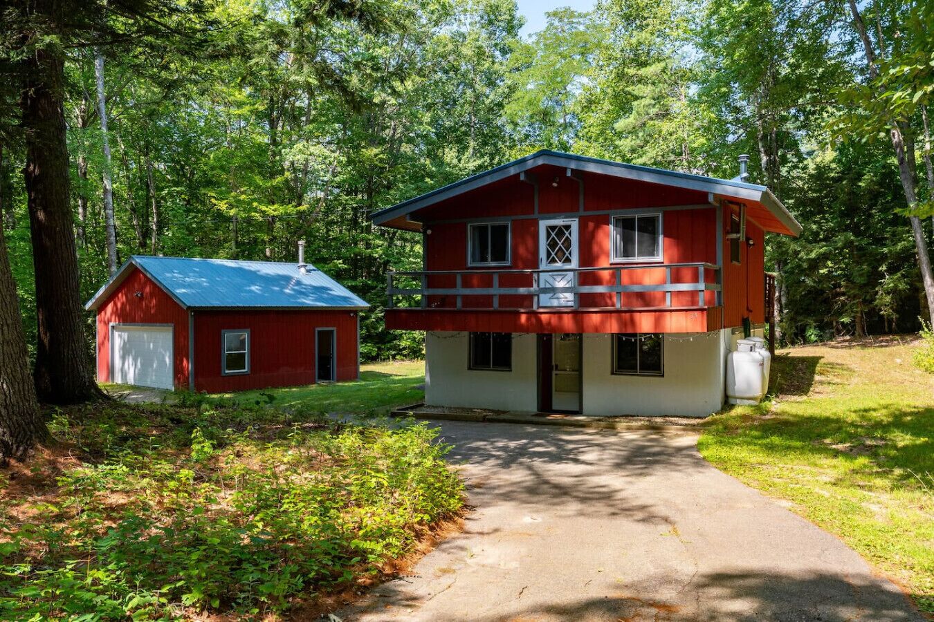 A two-story red and white cabin with a garage, surrounded by a forest.