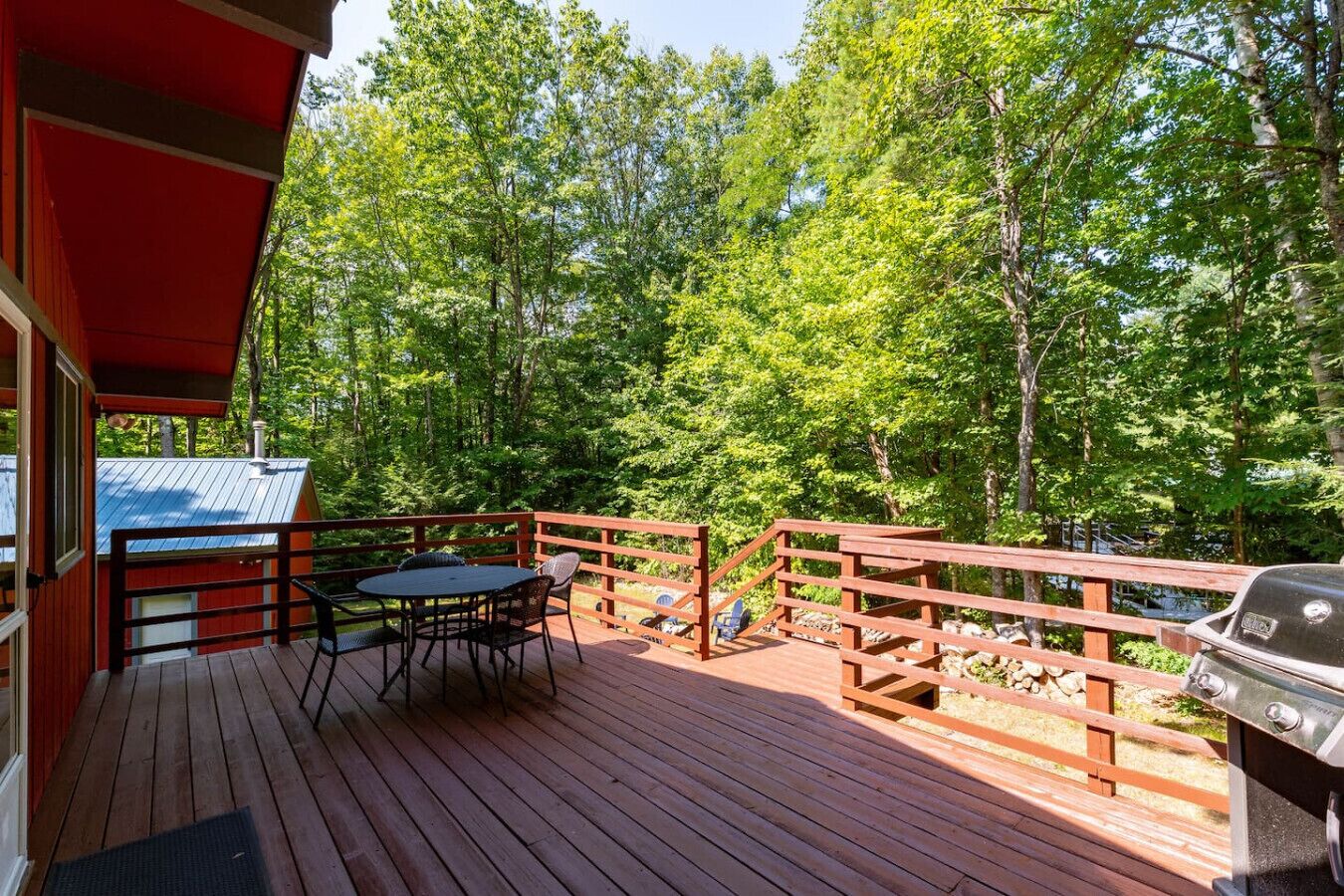 Une terrasse en bois, agrémentée d’une table et de chaises, entourée d’une balustrade en bois, et offrant une vue sur une zone boisée.