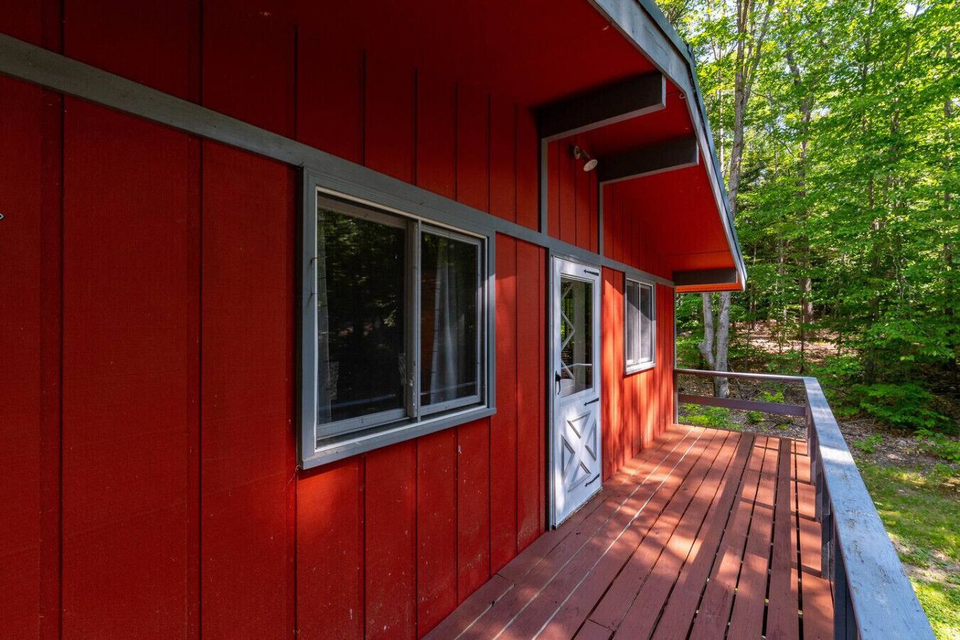 Eine rote Holzhütte mit einer Holzterrasse und einer Tür mit einem Fenster.