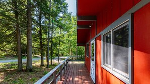 A red building with a wooden deck and a white railing, surrounded by trees. - Story Land- Fall Foliage - Attitash - Fire Pit (Bartlett)