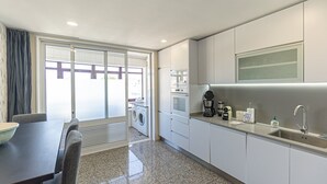 Een moderne keuken met inbouwapparatuur, een eethoek met tafel en stoelen, en uitzicht door een glazen deur op een terras.