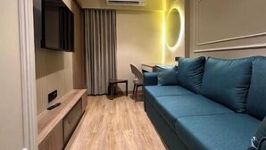 Un salon moderne avec un canapé bleu, un téléviseur à écran plat fixé au mur, un ventilateur de plafond et un appareil de climatisation.