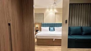 Une chambre d’hôtel moderne avec un plancher en bois, un lit doté d’une tête de lit bleue, un canapé vert et un ventilateur de plafond.