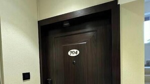 Une porte en bois sombre, portant le numéro 704, un petit objet carré noir fixé au mur sur la gauche, et un mur de couleur claire.