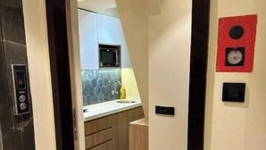 Un pasillo estrecho con una puerta de madera a la izquierda y una cocina visible al fondo.