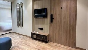 Una habitación moderna con un armario de madera, televisor montado y una zona de estar con un sofá y reposapiés azules.
