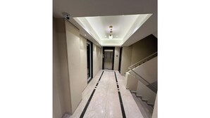 Un pasillo con piso de mármol, una escalera y un candelabro en el techo.