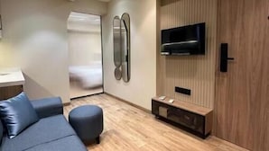 Una sala de estar moderna con sofá, reposapiés, suelo de madera, televisor montado en un panel de madera y ventilador de techo.
