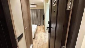 Un pasillo de hotel con suelo de madera, una cama con cortinas grises y una puerta con cerradura.