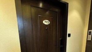 Una puerta de madera oscura con el número 703, una pared de color claro y un piso de mármol con una franja negra.