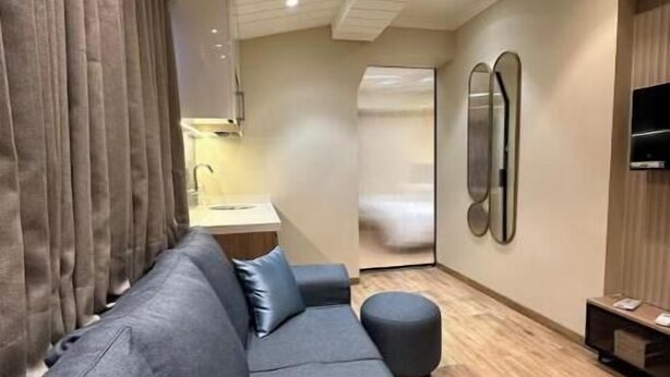 Una habitación moderna con un sofá gris, un pequeño otoman, piso de madera y un televisor montado en la pared.
