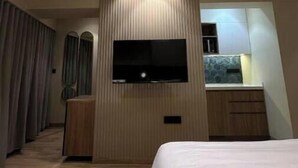 A modern hotel room with a bed, a flat-screen TV mounted on a wooden panel, a ceiling fan, and a small kitchenette area. - Skyline A : A Cozy Studio Apartment (Mumbai)