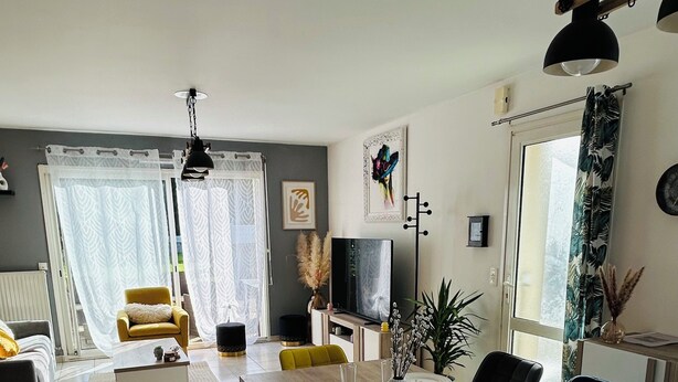 A modern living room with a sofa, a yellow armchair, and a dining area with a table set for two. - Penn-Ty: Cosy getaway in Brittany (Ploeren)