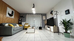 A modern living room with a grey sofa, a yellow armchair, a coffee table, a TV on a stand, and a potted plant. - Penn-Ty: Cosy getaway in Brittany (Ploeren)