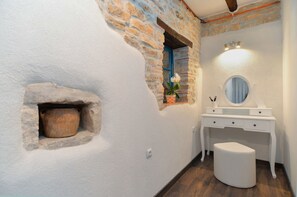 A bathroom with a stone wall, a wooden bucket, a white vanity with a mirror, and a small stool. - Holiday apartment with large garden and barbecue facilities (Mrgani)