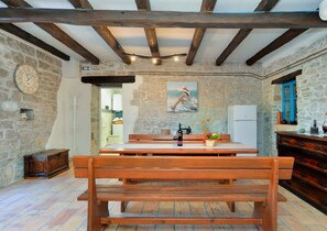 A rustic kitchen with exposed beams, a wooden bench, and a stone wall. - Holiday apartment with large garden and barbecue facilities (Mrgani)