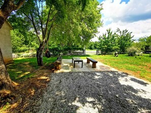 An outdoor seating area with a table and benches, surrounded by trees and a grassy lawn. - Holiday apartment with large garden and barbecue facilities (Mrgani)