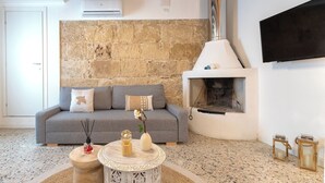 Ein Wohnzimmer mit Steinwand, grauem Sofa, Kamin und Wand-Fernseher.