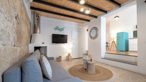 Ein modernes Wohnzimmer mit einem grauen Sofa, einem Kamin, einem Fernseher und einer durchgehenden Tür erkennbaren Küche.